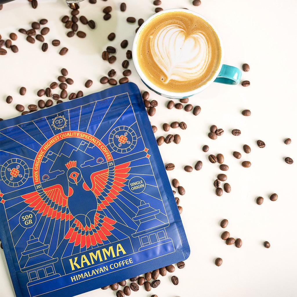 Kamma Himalayan Coffee package with a cup of coffee and scattered coffee beans on a white background