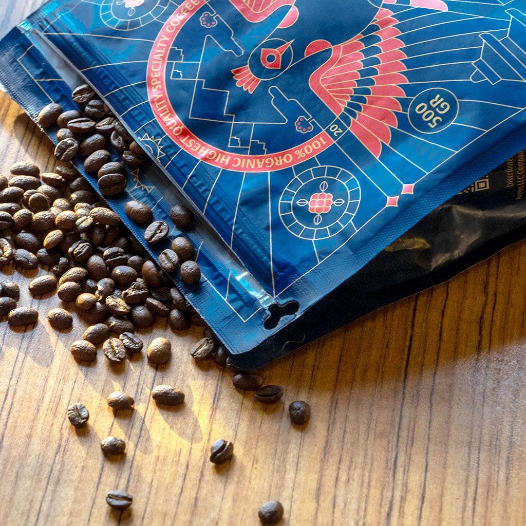 Blue coffee packaging with a red logo on a wooden surface with scattered coffee beans.